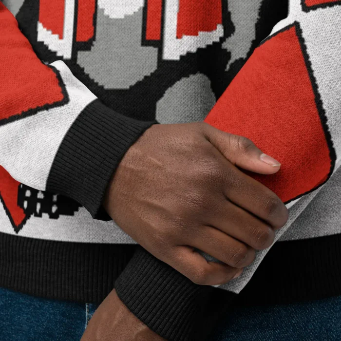 A close up of folded hands, and a knitwear sweatshirt with the colors red, black, white, and grey.