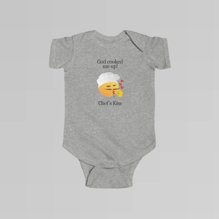 The front of a heather colored baby onesie with the words "God cooked me up!" above a version of the Chef's Kiss emoji. Beneath the emoji, the words "Chef's Kiss" are written.