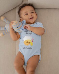 Another cute baby in a light blue onesie showcasing the Chef's Kiss Onesie, and holding a crocheted bear.