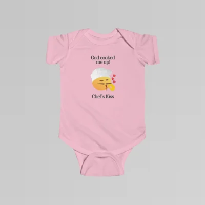 The front of a pink colored baby onesie with the words "God cooked me up!" above a version of the Chef's Kiss emoji. Beneath the emoji, the words "Chef's Kiss" are written.