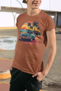 Younger Male showcasing the front of an autumn colored t-shirt with a classic retro vibe, and a classic car with palm trees and mountains in the background.