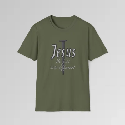 Military Green colored softstyle tee, with a crucifixion spike, and the name "Jesus" in big print over top of it. Beneath Jesus, it says "He just hits different", in a cursive font. The font is silver, with a dark grey border.