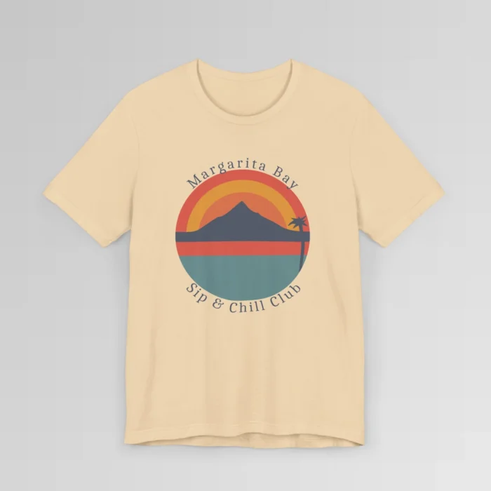 A soft cream colored t-shirt mockup (front) with a circular, minimalistic design of water, sky, mountains, and a palm tree. The colors are orange, yellow, deep blue, and blue. The tee has the words "Margarita Bay" and "Sip & Chill Club" wrapped around the circular design.