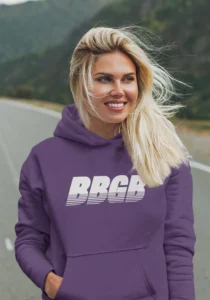 A female model wearing the BBGB Simple Hoodie Dark Colors, Purple, while walking down the middle of a road, smiling.