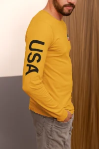 Right side view of male model wearing a gold colored "BBGB USA Full Stack Long Sleeve" Tee.