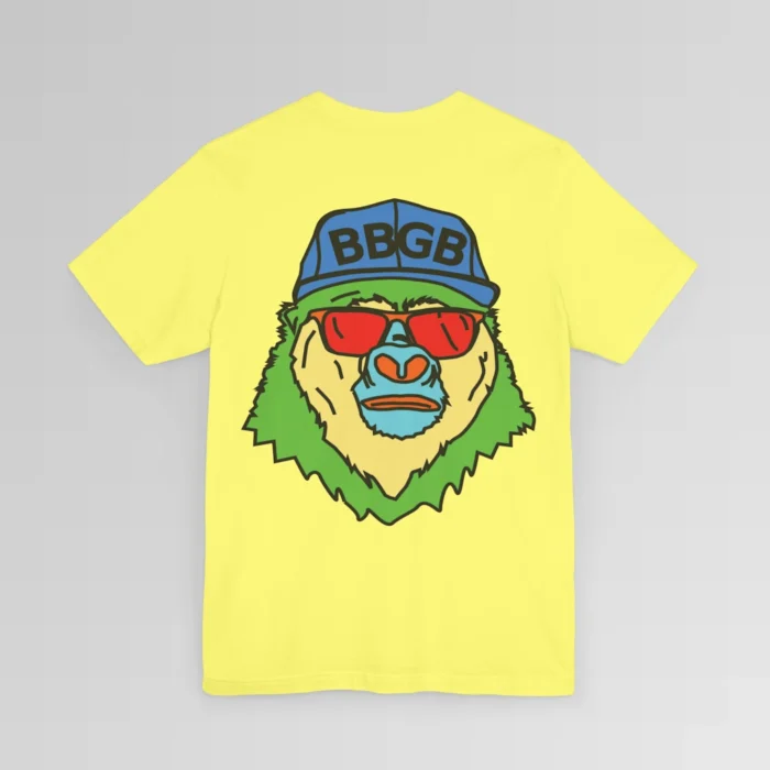 The back of a daisy colored shirt, with the Big Baby Gorilla Bear Mascot's face in vibrant colors of light blue, green, yellow, and orange, wearing a blue ball cap, and red shades, super imposed on the back of a t-shirt.