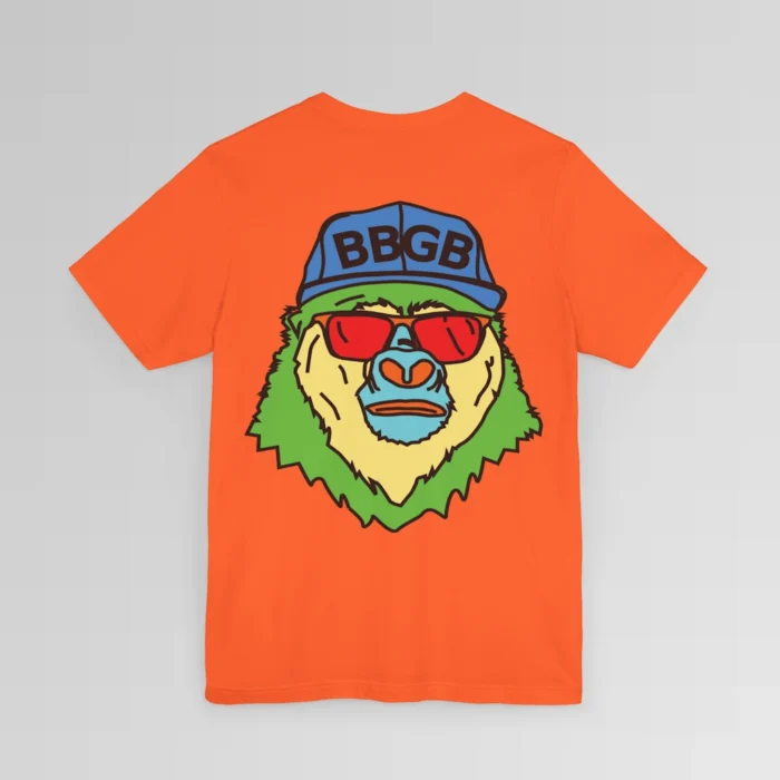 The back of an orange colored shirt, with the Big Baby Gorilla Bear Mascot's face in vibrant colors of light blue, green, yellow, and orange, wearing a blue ball cap, and red shades, super imposed on the back of a t-shirt.