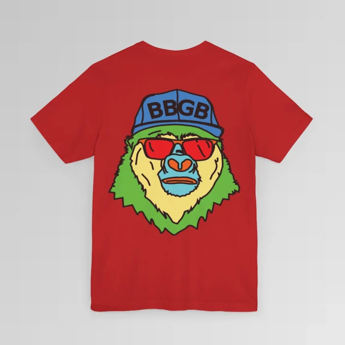 The back of a red colored shirt, with the Big Baby Gorilla Bear Mascot's face in vibrant colors of light blue, green, yellow, and orange, wearing a blue ball cap, and red shades, super imposed on the back of a t-shirt.