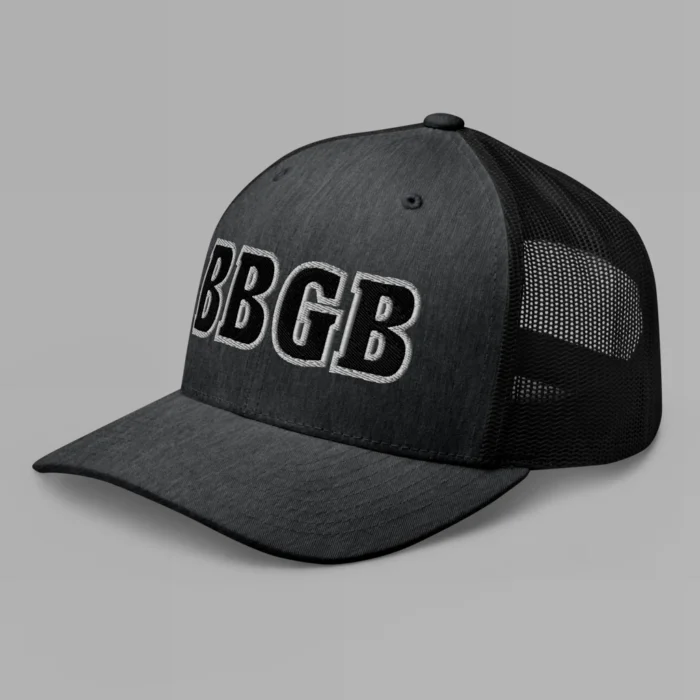 A dark heather grey hat with the letters "BBGB" embroidered on the front in black thread, with a white border, on a trucker cap with a mesh back. (Left Side View)