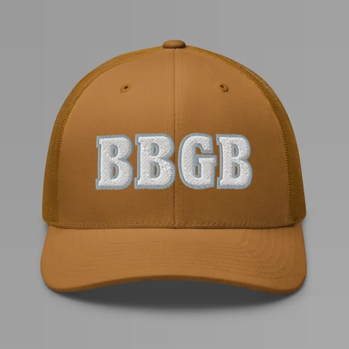 A caramel colored hat with the letters "BBGB" embroidered on the front in white thread, with a silver border, on a trucker cap with a mesh back.