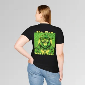 Female model in black t-shirt showing the back of a tee with a green and gold graphic of a swag looking gorilla bear character, wearing shades, with a sun behind it, in a retro style, and the words "The King" and "Mardi Gras" in a gradient colored yellow to green font.