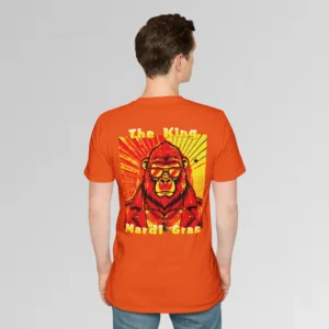 Male model in orange t-shirt showing the back of a tee with a green and gold graphic of a swag looking gorilla bear character, wearing shades, with a sun behind it, in a retro style, and the words "The King" and "Mardi Gras" in a gradient colored yellow to green font.