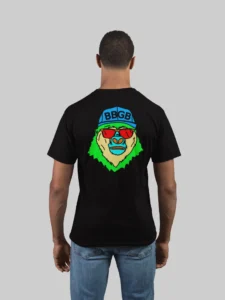 Male model showcasing the back of a black colored tee, with the Big Baby Gorilla Bear Mascot's face in vibrant colors of green, yellow, blue, and orange.., wearing a blue ball cap and red shades, super imposed on the back of a t-shirt.