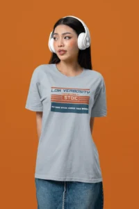 Female wearing headphones, a jean skirt, and the "Low Verbosity" tee by Big Baby Gorilla Bear - Light Blue, with an orange background.