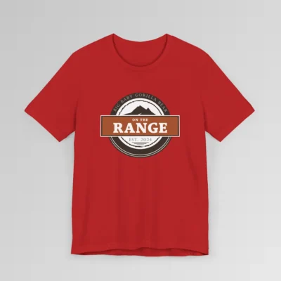 The front of a shirt with a dark brown, and cream white circular design, with the words "Big Baby Gorilla Bear" wrapped on the top part of the circle, and "Est. 2024" on the bottom inner part of the circle. In the center, there is an orange and brown rectangle with the words "On The Range", and a mountain graphic. Color = Red.