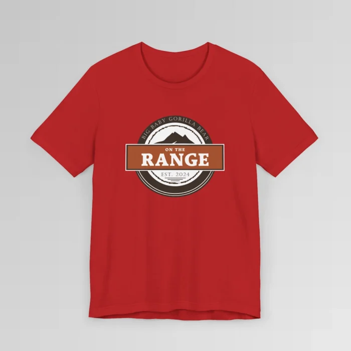 The front of a shirt with a dark brown, and cream white circular design, with the words "Big Baby Gorilla Bear" wrapped on the top part of the circle, and "Est. 2024" on the bottom inner part of the circle. In the center, there is an orange and brown rectangle with the words "On The Range", and a mountain graphic. Color = Red.
