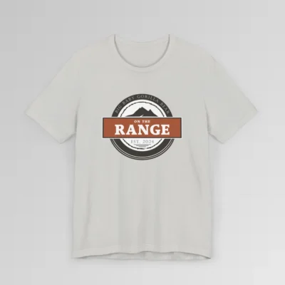 The front of a shirt with a dark brown, and cream white circular design, with the words "Big Baby Gorilla Bear" wrapped on the top part of the circle, and "Est. 2024" on the bottom inner part of the circle. In the center, there is an orange and brown rectangle with the words "On The Range", and a mountain graphic. Color = Silver.