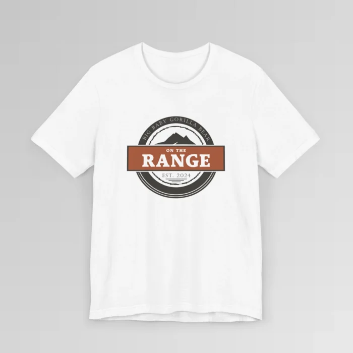 The front of a shirt with a dark brown, and cream white circular design, with the words "Big Baby Gorilla Bear" wrapped on the top part of the circle, and "Est. 2024" on the bottom inner part of the circle. In the center, there is an orange and brown rectangle with the words "On The Range", and a mountain graphic. Color = White.