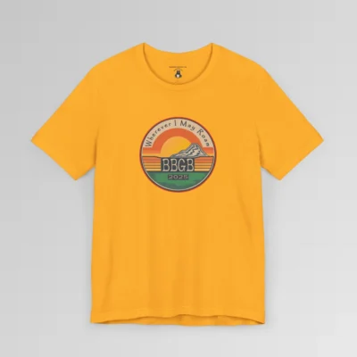 The front of a gold tee. with a circular, retro sunset design, with mountains, the letters "BBGB", "2025" in the middle, and the words "Wherever I May Roam" on the top of the circle. Red, Deep blue, teal, orange, yellow, and cream colors in the design.