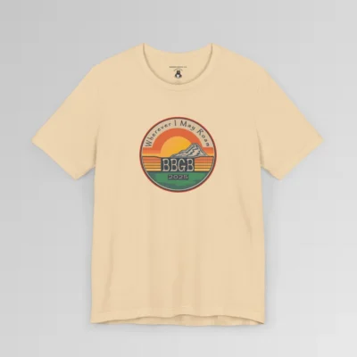 The front of a soft cream tee. with a circular, retro sunset design, with mountains, the letters "BBGB", "2025" in the middle, and the words "Wherever I May Roam" on the top of the circle. Red, Deep blue, teal, orange, yellow, and cream colors in the design.