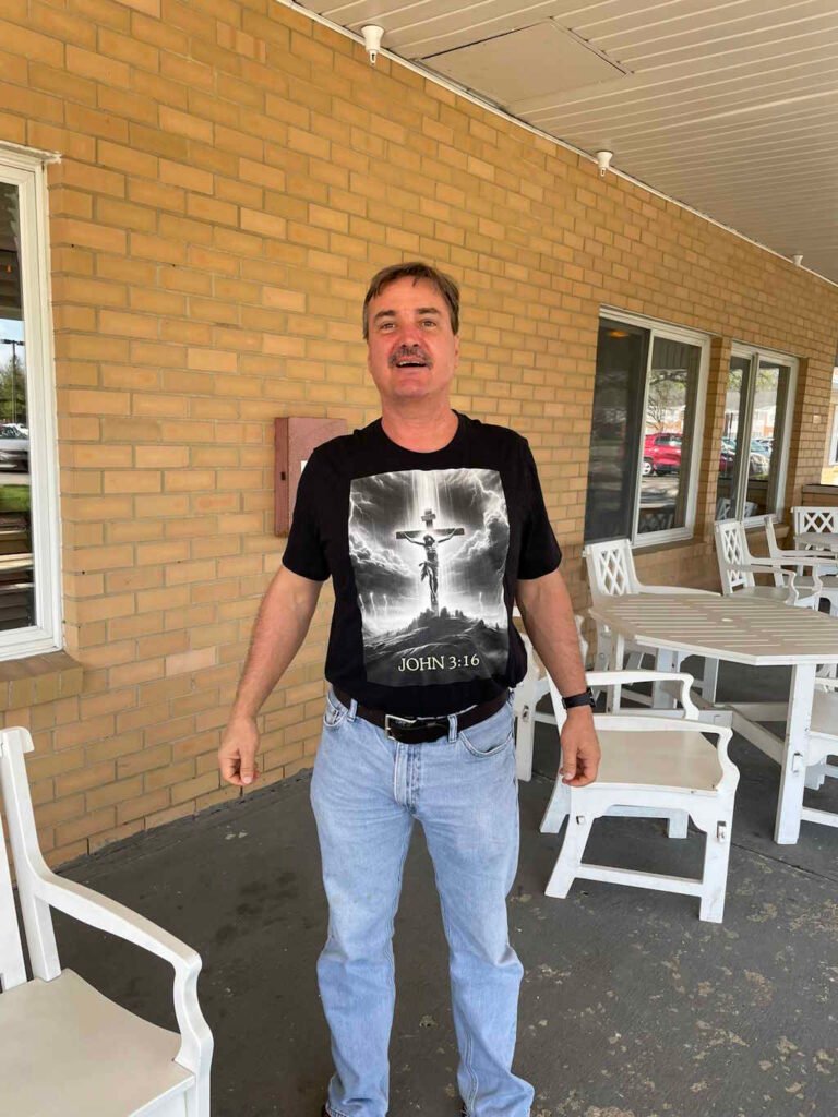 Male wearing a BigBabyGorillaBear.Com black t-shirt with an image of Christ on the cross a reference to the verse in the Bible - John 3:16