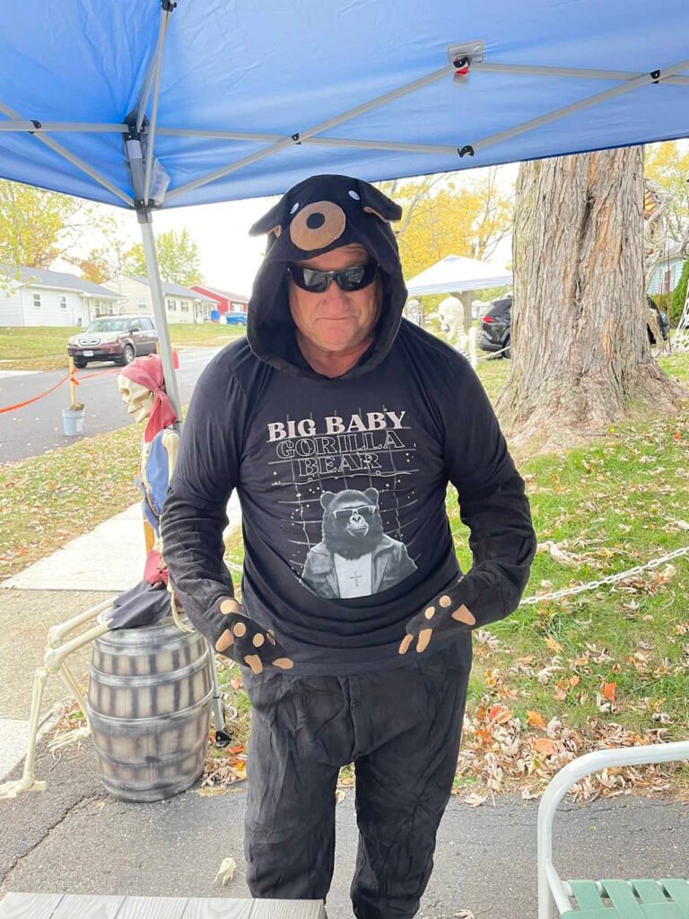 A male wearing a playful bear costume and the Big Baby Gorilla Bear retro styled tee - black - standing outside under a tent.