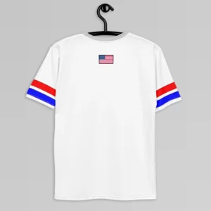 The backside of the New York United States Luxurious Tee, white, on a hanger. The shirt has a light grey collar, red and blue stripes on the sleeves with a black outline, and the American flag in the top, center of the tee.